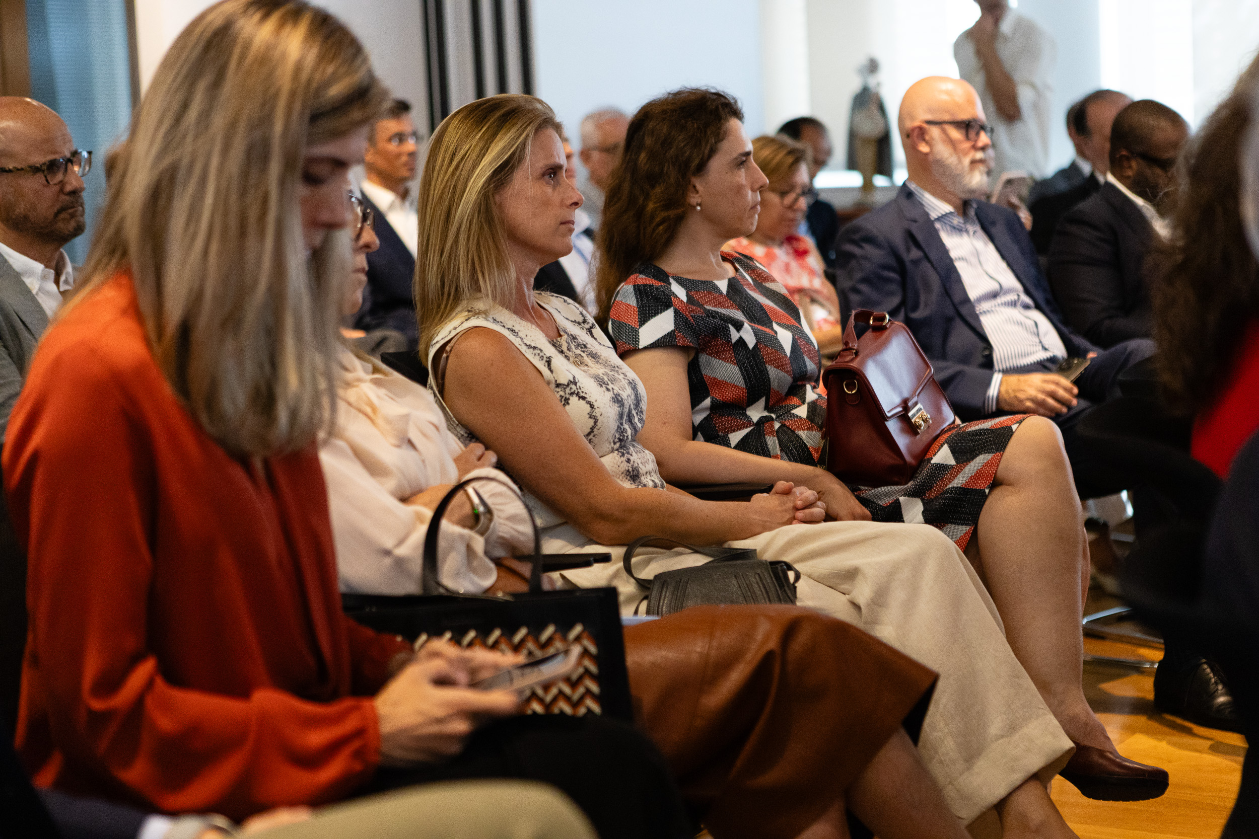 Audience of professionals seated in a conference room, attentively listening to a presentation in front of them.