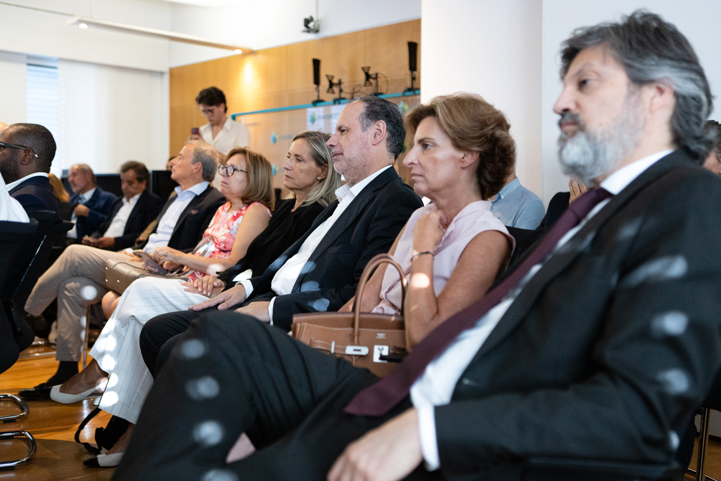 Group of professionals seated in a conference room, attentively listening to a presentation in business attire.