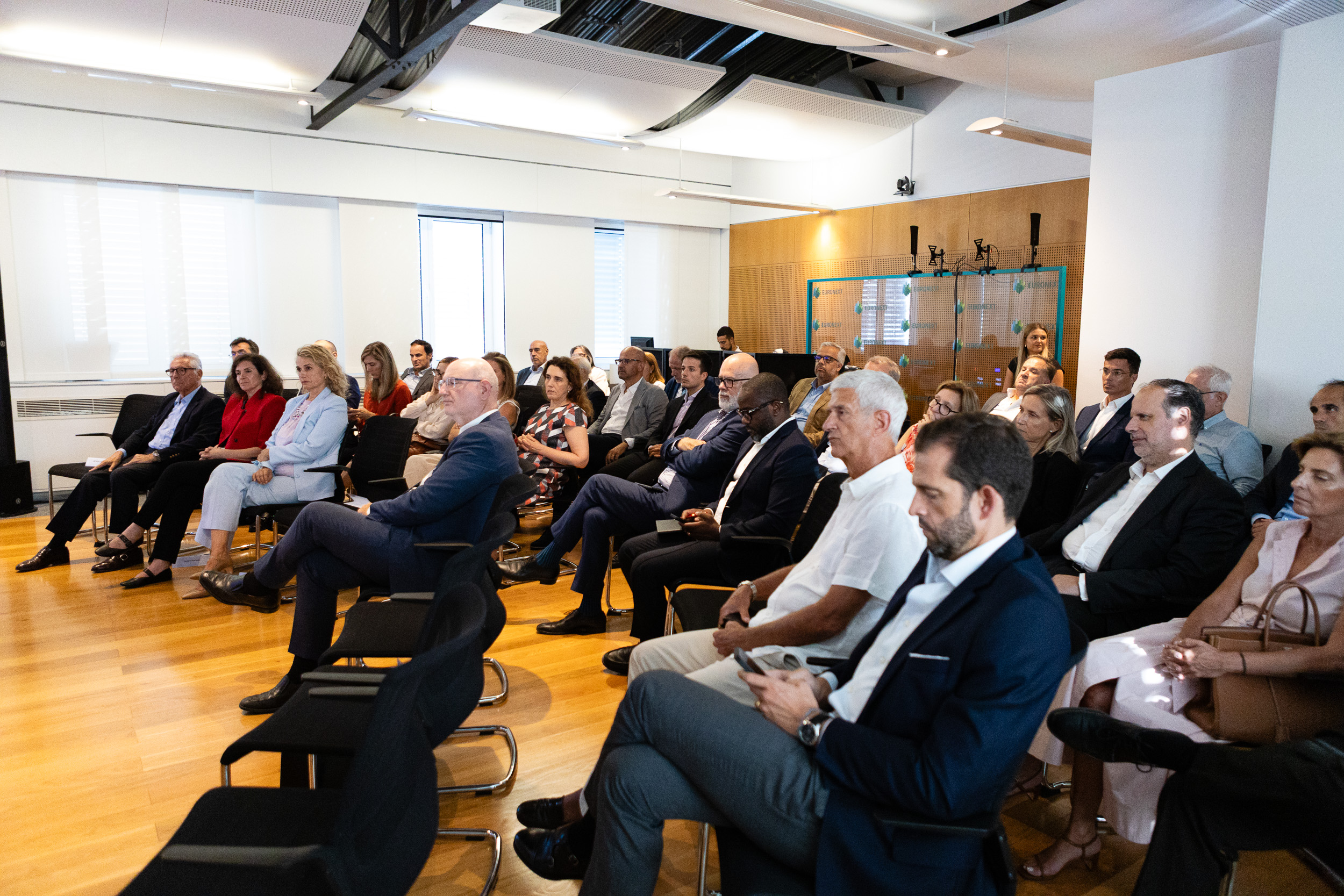 Group of business professionals seated in a bright meeting room, attentively listening to a presentation.