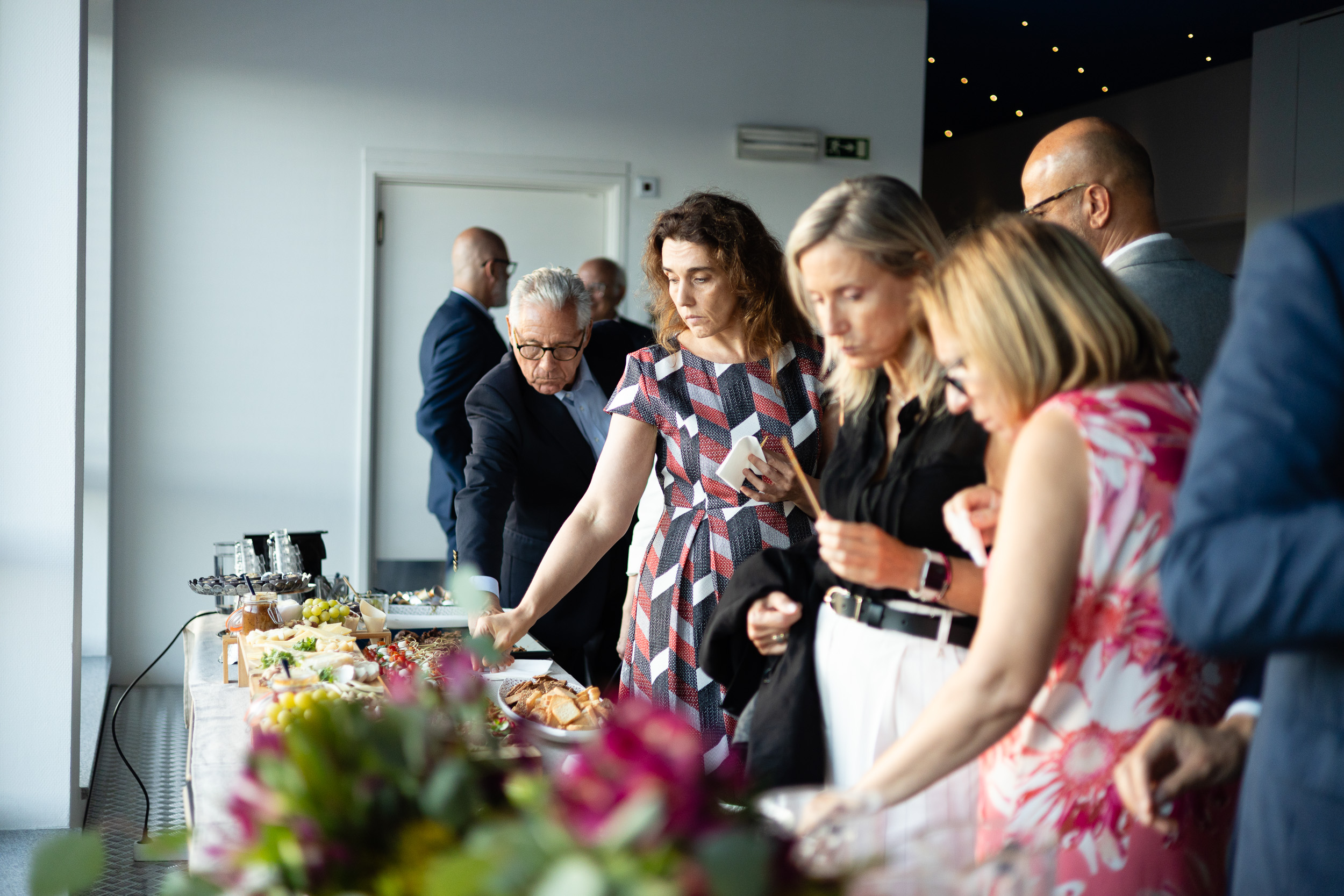 Professionals in business attire serving themselves from a buffet table with appetizers and drinks in a modern venue