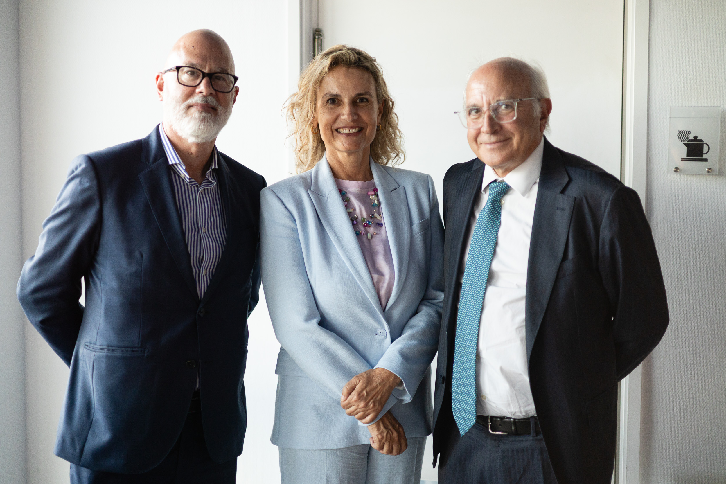 Three professionally dressed colleagues posing together and smiling in a doorway.