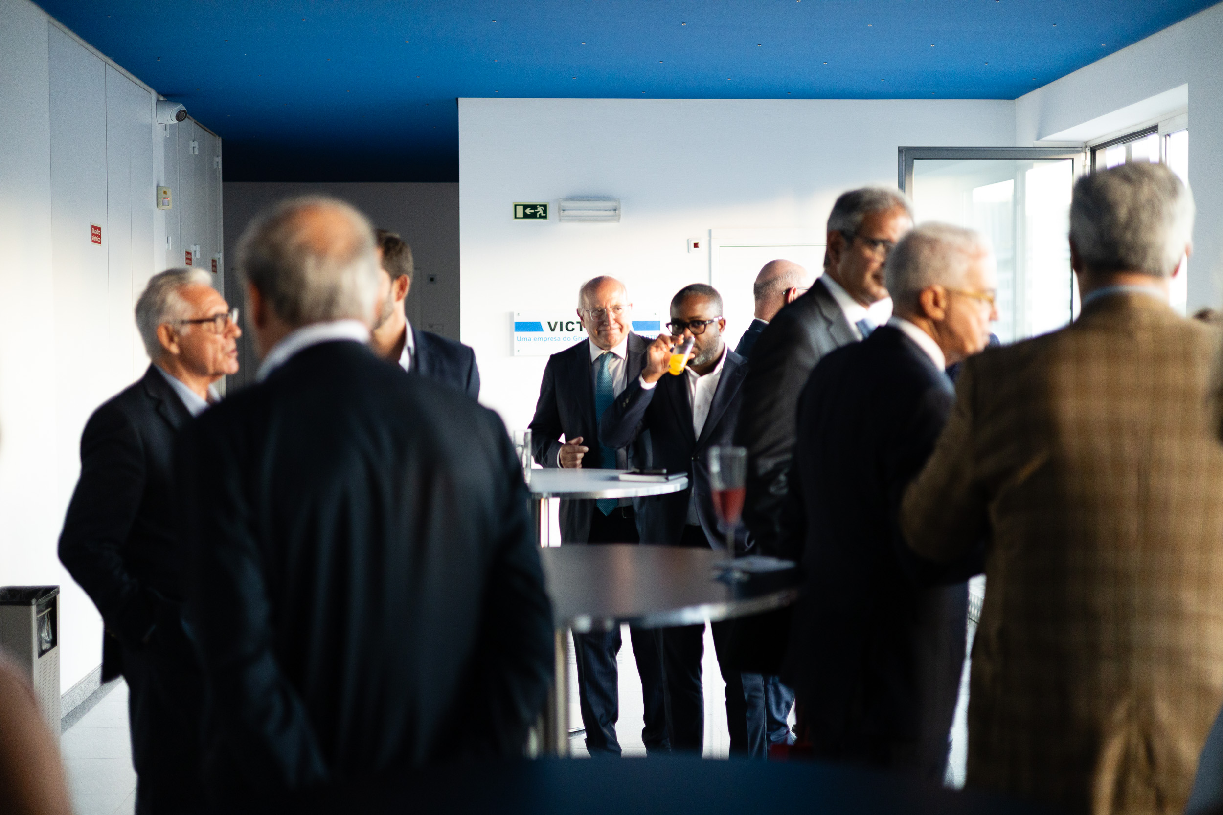 Group of professionals in business attire socializing at a modern office lounge with drinks on a high table.