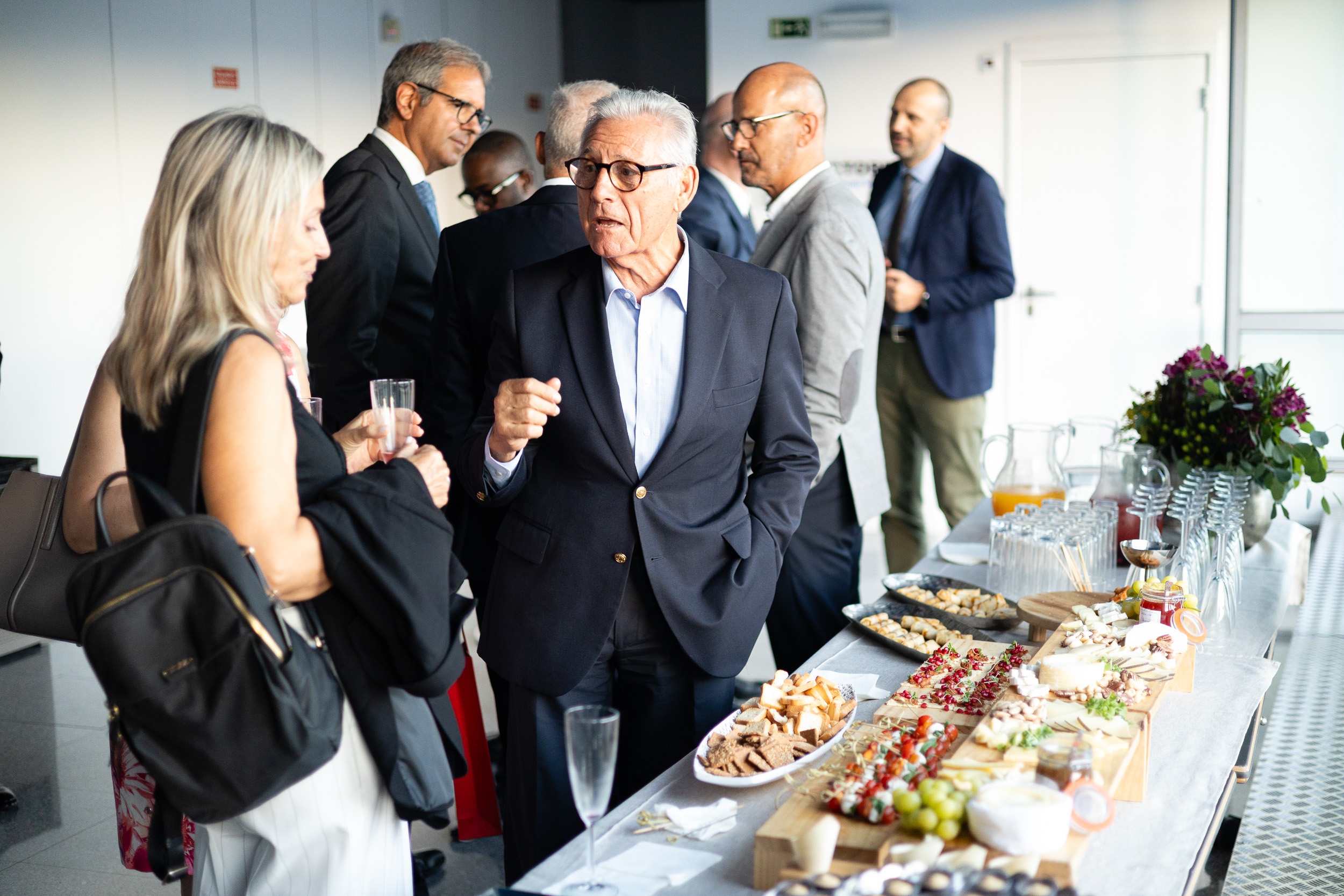 Group of professionals in business attire socializing at a catered reception with a spread of appetizers on a long table