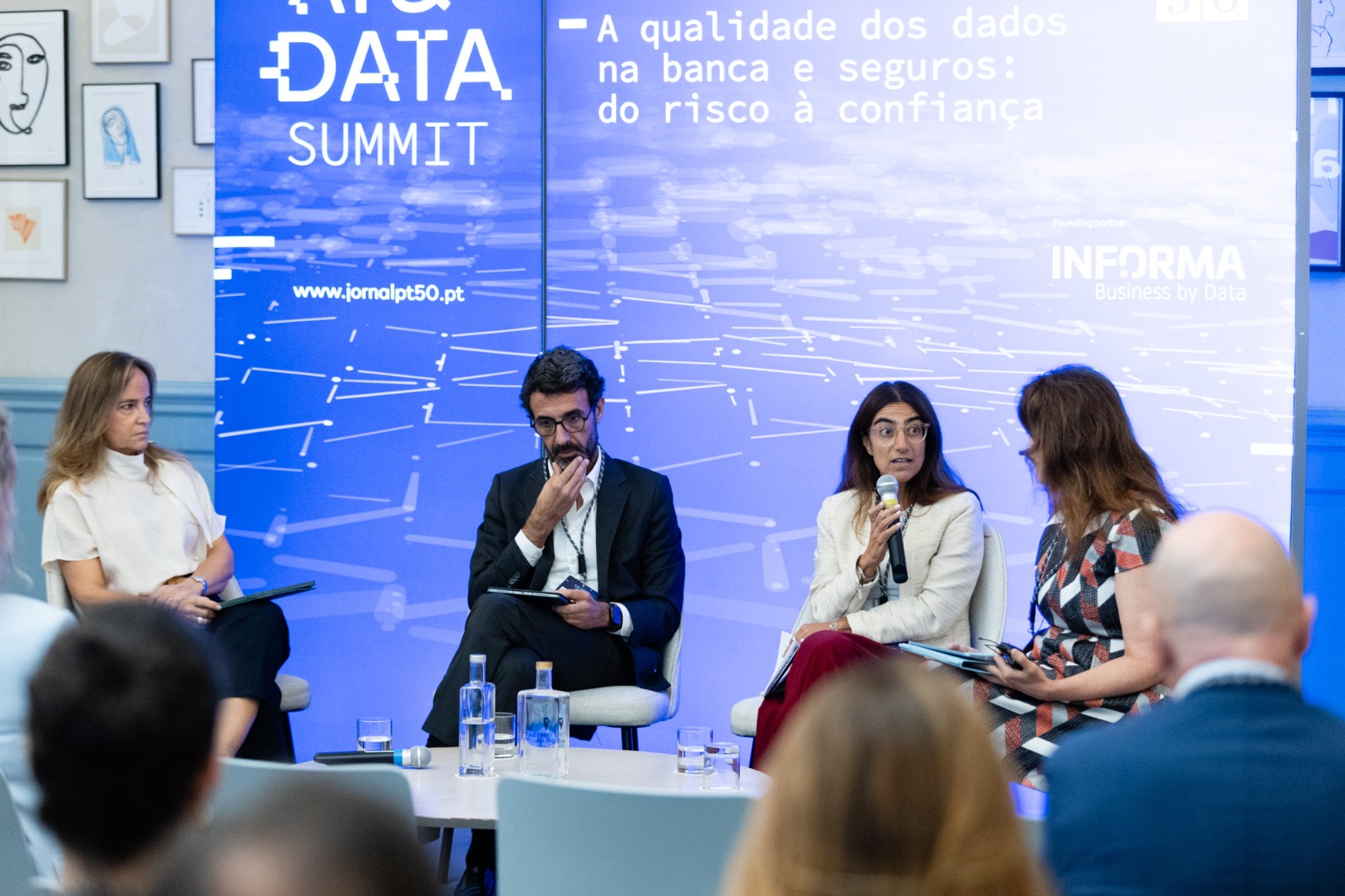 Panel discussion at a data summit: four speakers on stage, with a blue backdrop that reads 'DATA SUMMIT'; a woman speaks into a microphone while others listen.